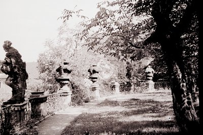 Classic Baroque-style garden pathway lined with ornate stone urns and statues, evoking 18th-century European estate design. O...