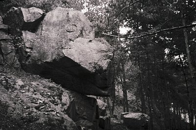 High-contrast black-and-white shot of a **stone carving** resembling a reclining human figure integrated into a rocky cliff f...