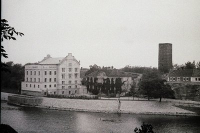 Historic brick building complex by a river, featuring neoclassical architecture with arched windows and a prominent chimney. ...