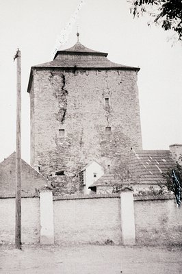 Historic stone watchtower with octagonal turret, weathered brickwork, and small slit windows. Whitewashed fence and adjacent ...