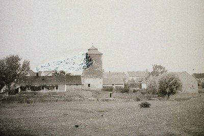 Rural scene featuring a stone tower with a conical roof, likely a windmill or dovecote. Surrounding buildings suggest a small...