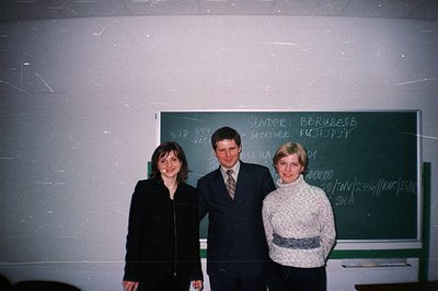 Three individuals pose in what appears to be an office or classroom setting, circa 1990s. Two women wear professional attire;...