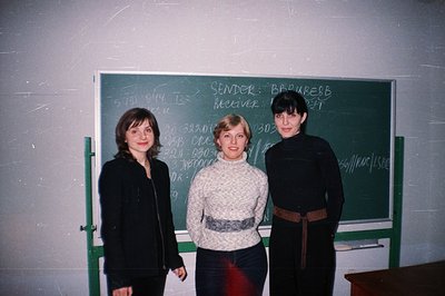 Three young women stand posed before a green chalkboard covered in handwritten notes and numbers, possibly an academic or bur...