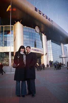 A couple stands in front of the Varna railway station in Bulgaria. The station's modern, glass-facade architecture is promine...