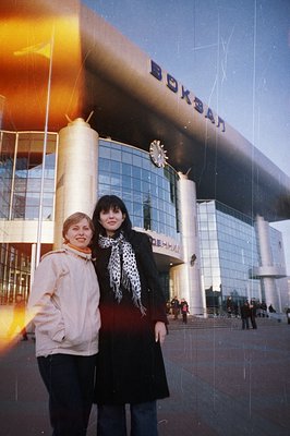 Two women stand outside Varna railway station, Bulgaria. Brutalist architecture dominates; signage and a large clock visible....