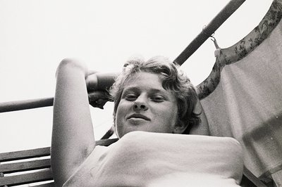 Close-up, black and white portrait of a young woman reclining on a striped fabric surface. She appears relaxed, eyes closed, ...