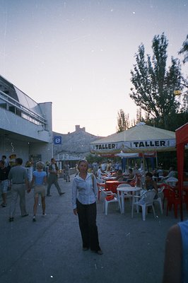 A pedestrian promenade scene with a woman in focus, likely a tourist, framed against a background of restaurants and shops. W...