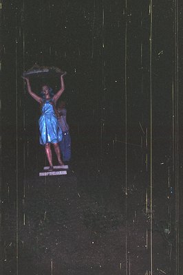 Statue of a woman, draped in blue, appears to float above a base. Likely a theatrical or promotional display. Unusual lightin...