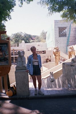 A young woman in athletic wear stands before ancient Egyptian statues, likely at a museum or historical site. She wears a den...
