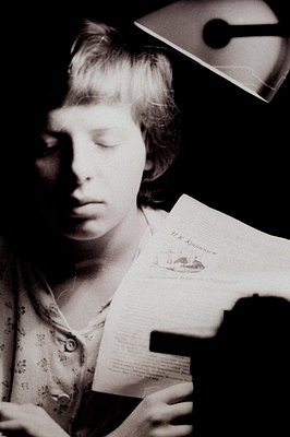 Close-up black & white portrait of a young girl, eyes closed, holding a document/book with printed text. Appears to be a cand...