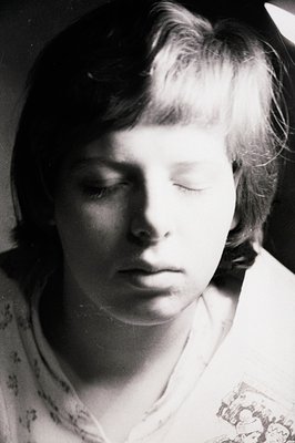 Close-up, black and white portrait of a young person with short, textured hair. Direct lighting creates strong shadows emphas...