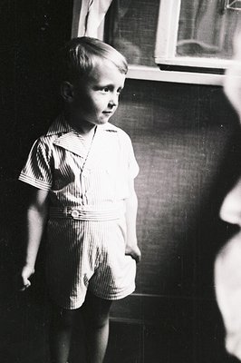 Striking black and white portrait of a young boy in striped shortalls, captured in a domestic setting. Subject appears contem...