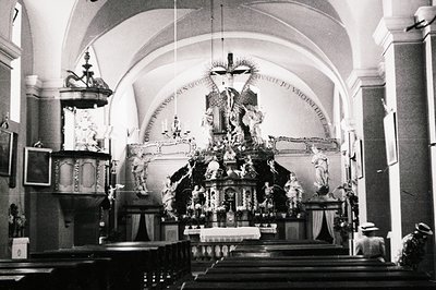 Ornate, dark interior of a Catholic church. A large, baroque altar features a crucifix and sculpted figures beneath a gilded ...