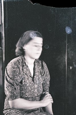 Black and white portrait showing a seated woman in a patterned blouse, hands clasped in her lap. Slightly blurred focus sugge...