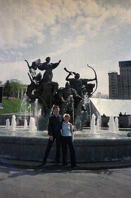 Monumental bronze sculpture of a warrior with a bow stands within a circular fountain, likely depicting a mythical figure. A ...