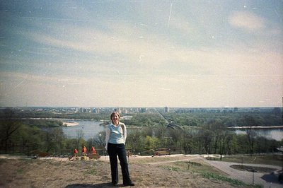 A woman stands on a grassy hillside overlooking a river valley and distant city. Likely taken in the 1970s, possibly Eastern ...