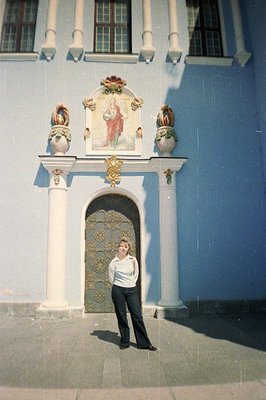 An exterior view features a woman in a white sweater and wide-leg trousers posed before an ornate building entrance. The faca...