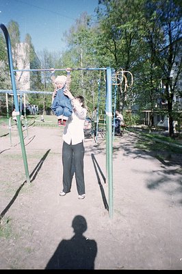 A man lifts a young child while standing on a playground, likely a father-child moment. The playground features climbing fram...