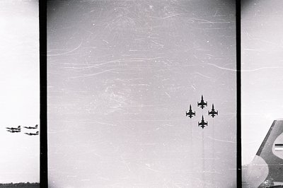 Monochrome aerial view captures a four-plane aerobatic team in flight, likely a military demonstration. Visible scratches and...