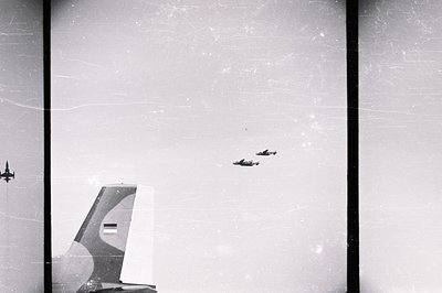 A trio of aircraft fly in formation against a cloudy sky. A portion of a large airplane's tail fin, marked with the flag of A...