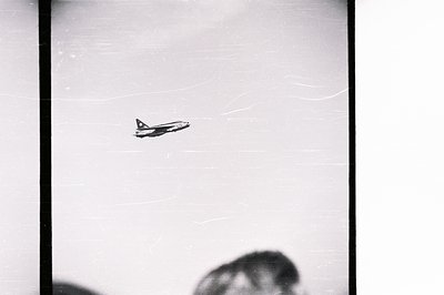 A sharply focused, angled view captures a military aircraft in flight against a bright sky. The plane’s markings suggest pote...