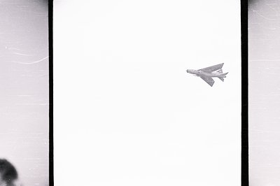 Monochrome image captures a fighter jet in flight, likely a McDonnell Douglas F-4 Phantom. Visible details include wing-mount...