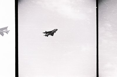 Striking black & white image captures a fighter jet in flight, likely a MiG-17 or similar Cold War-era design. Visible markin...