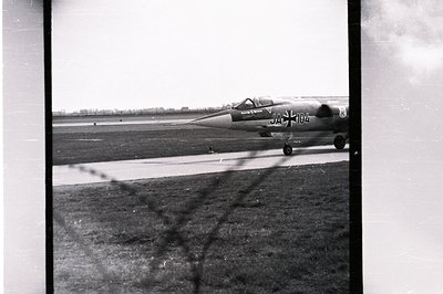 Black and white image depicts a fighter jet, possibly a MiG, taxiing on an airfield. Visible markings "JA-104" and a Cyrillic...
