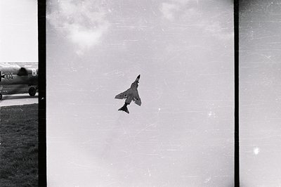 A fighter jet, likely an F-4 Phantom, performs a dramatic maneuver against a cloudy sky. The plane is angled sharply, showcas...