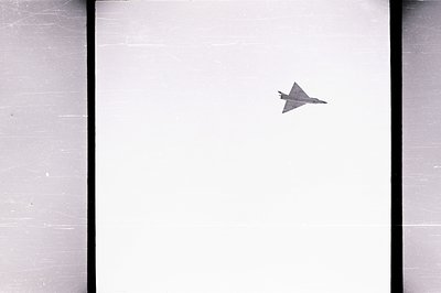 Striking aerial view of a delta-winged aircraft, likely a Mirage fighter jet, in flight. The stark white sky provides minimal...