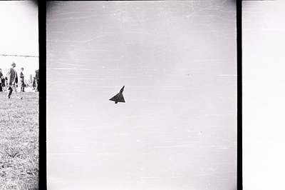 A paper airplane soars across the frame. A small group of children, bundled in outerwear, are visible in the lower left corne...