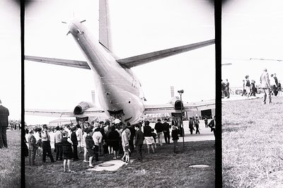 A large crowd gathers around a parked Tupolev Tu-134 airliner. The aircraft’s tail dominates the frame, showcasing its distin...