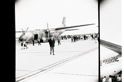 A military transport aircraft stands on a tarmac, likely during an open house or demonstration. A man in a suit approaches th...