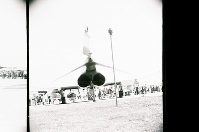 A Soviet-era MiG-21 fighter jet stands prominently on display, flanked by spectators. Likely an airshow or military exhibitio...