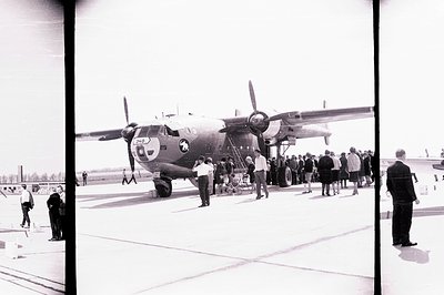 A Douglas C-47 Skytrain aircraft sits on a tarmac, with a crowd of onlookers gathering nearby. Visible markings indicate US A...