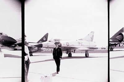 A uniformed officer walks past an F-104 Starfighter aircraft on a tarmac. Multiple aircraft are visible in the background. Li...