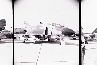 An A-7D Corsair II aircraft sits on a tarmac, loaded with ordnance. Detail shows its distinctive nose and wing shape. A lone ...