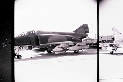 A US Navy Douglas A-4 Skyhawk aircraft sits on a concrete tarmac. Equipped with underwing ordnance, the plane displays visibl...