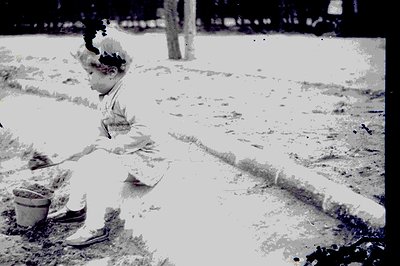 Vintage black and white photo depicts a young child, likely a toddler, playfully interacting with a small bucket and what app...