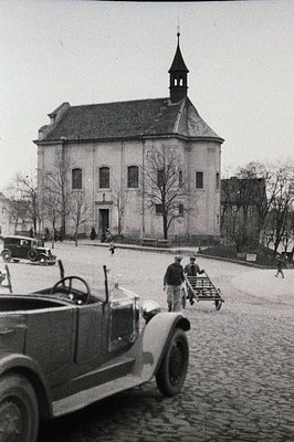 A stately building, possibly a church or public hall, dominates the view, its facade symmetrical with arched windows. A vinta...