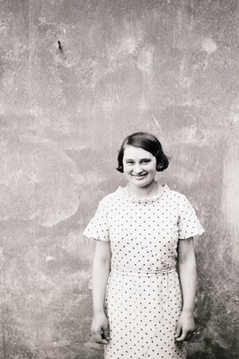 Young woman in a spotted dress poses directly to camera, exhibiting a cheerful expression. Short, dark hair styled in a bob. ...