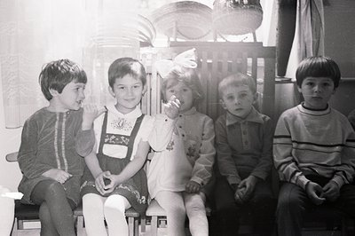 Five children, likely siblings, sit formally in what appears to be a traditional interior. The girl in the center wears a dir...
