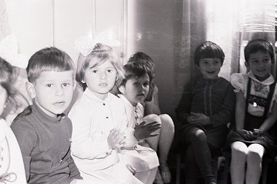 Group portrait of five young children, likely in a school or childcare setting. A girl with a bow in her hair stands in front...
