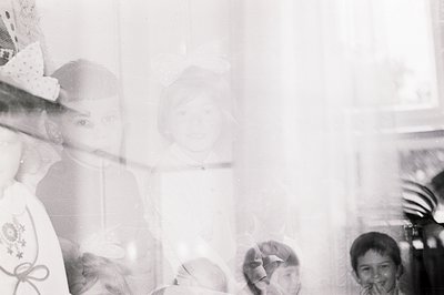 A grainy, black and white photograph shows children pressed against a window. Several wear what appear to be festive hats wit...