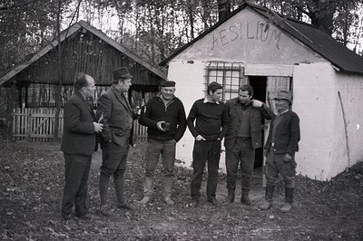 Five men stand before a small, whitewashed building labeled "Aesilium," seemingly in a rural setting. The men are dressed in ...
