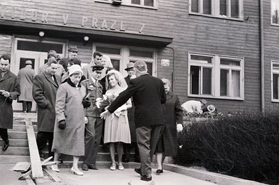 A crowd gathers outside a building identified as "JRD Prague 7," likely a post office. A woman in a light-colored dress and h...