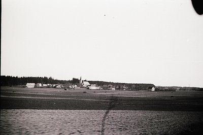 A coastal townscape, likely Eastern Europe, viewed across a wide expanse of water. Buildings with simple architecture are clu...