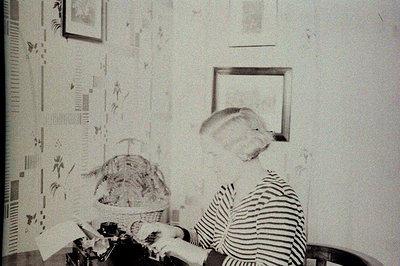A woman seated at a desk, meticulously working with photographic printing chemicals in a darkroom. Wallpaper with a geometric...