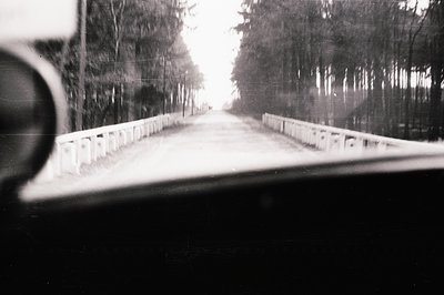 Dramatic, blurred roadside scene captured from a moving vehicle. Concrete guardrail visible alongside a road receding toward ...