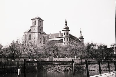 Grand, imposing monastery complex with a prominent tower and baroque dome architecture rises from a hillside. The structure f...